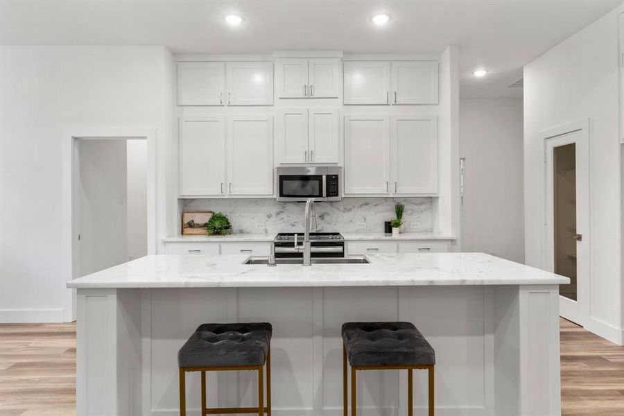 Kitchen with a center island with sink, light stone counters, stainless steel appliances, and white cabinets