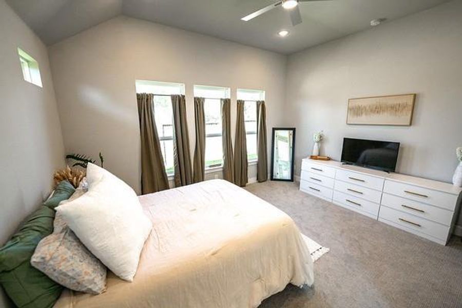 Bedroom featuring ceiling fan, light carpet, vaulted ceiling, and multiple windows