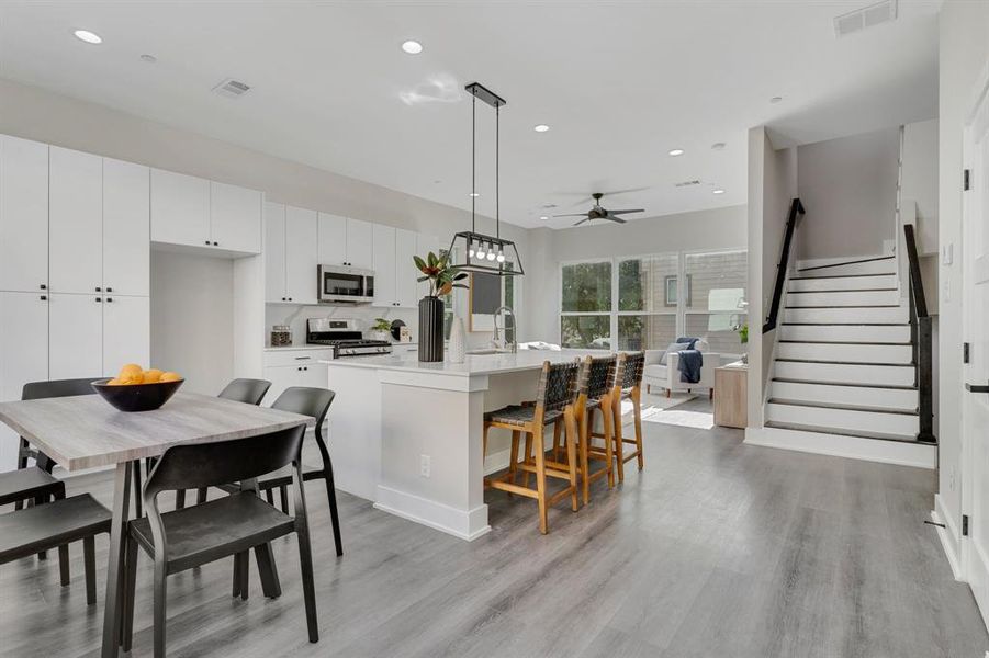 Kitchen with light wood-type flooring, ceiling fan, an island with sink, appliances with stainless steel finishes, and pendant lighting