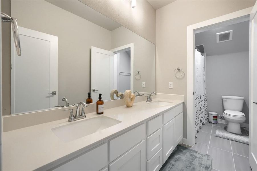 Bathroom with tile floors, double sink, toilet, and vanity with extensive cabinet space