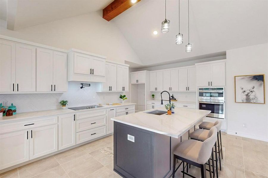 Kitchen featuring white cabinets, beamed ceiling, a center island with sink, and sink