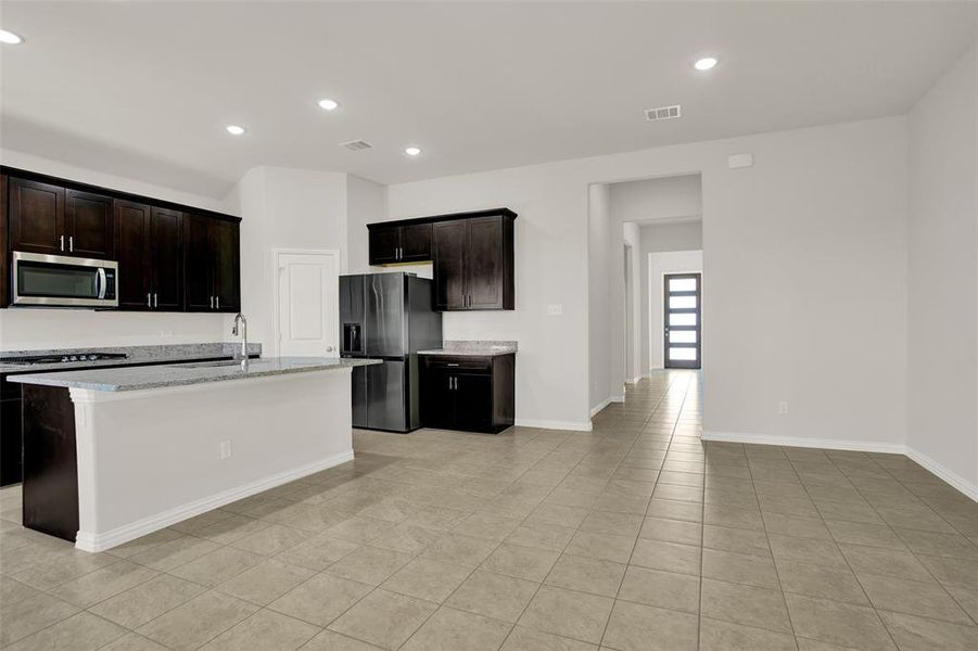 Kitchen featuring light tile floors, a kitchen island with sink, light stone counters, and stainless steel appliances
