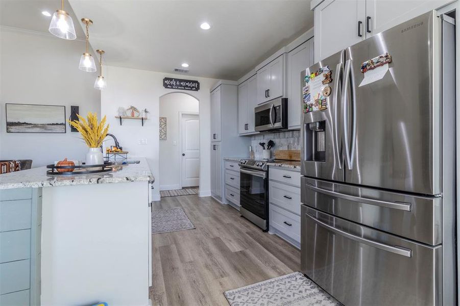 Kitchen featuring cabinetry, stainless steel appliances, hanging light fixtures, and light hardwood / wood-style flooring