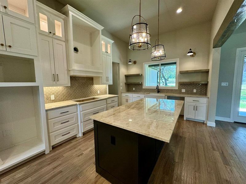 Kitchen featuring light stone counters, white cabinets, a kitchen island, dark wood-type flooring, and stovetop