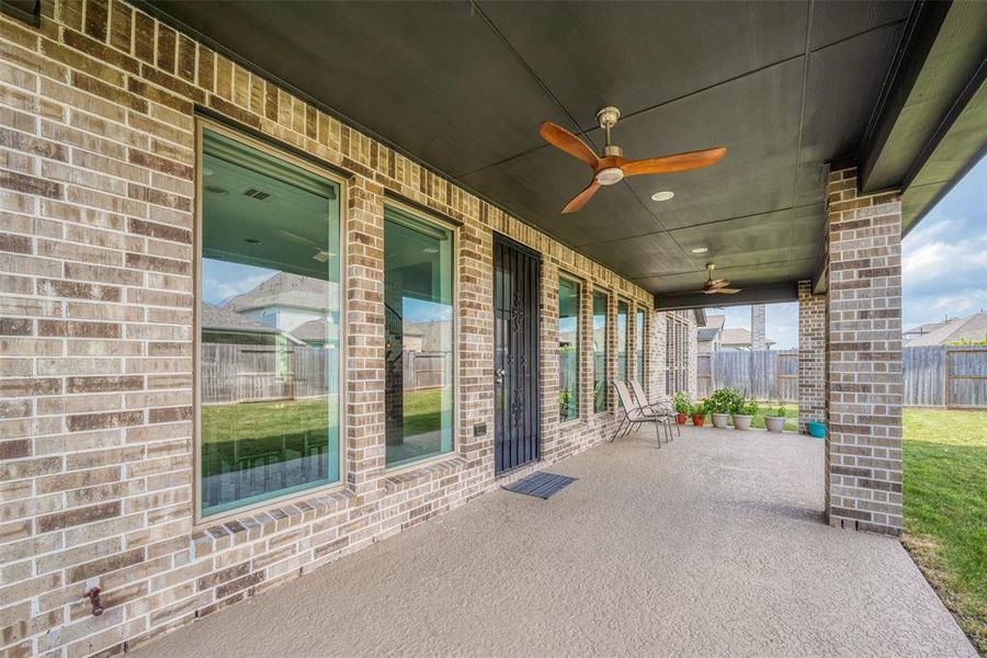 This photo showcases a spacious covered patio with a brick exterior, ceiling fans for comfort, and large windows providing natural light and views of the backyard. Perfect for outdoor relaxation and entertainment.