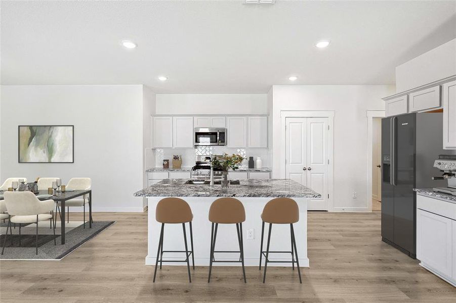 Kitchen with stainless steel appliances, light stone countertops, light hardwood / wood-style flooring, and a center island with sink