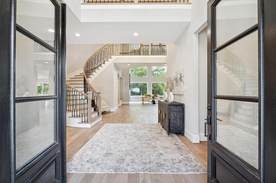 This elegant entryway features a sweeping staircase with modern wrought iron balusters, high ceilings, and a bright, open layout leading into a spacious living area and offering a sophisticated welcome to a stunning home.