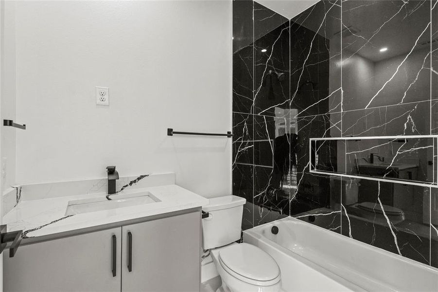 Full bathroom with tiled shower / bath combo, vanity, and toilet