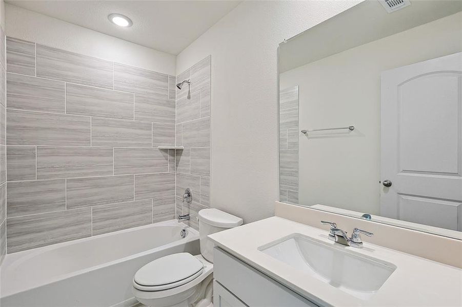 Full bathroom featuring vanity, tiled shower / bath combo, and toilet