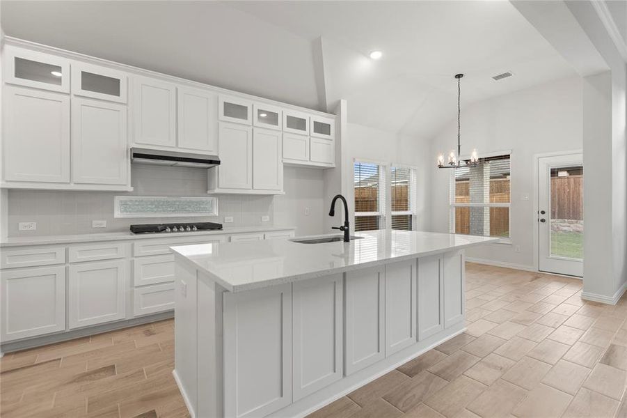 Kitchen featuring decorative backsplash, a healthy amount of sunlight, vaulted ceiling, and a kitchen island with sink