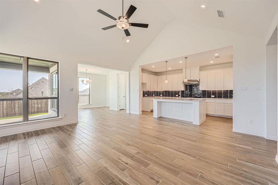 Unfurnished living room with ceiling fan with notable chandelier, high vaulted ceiling, and light hardwood / wood-style floors