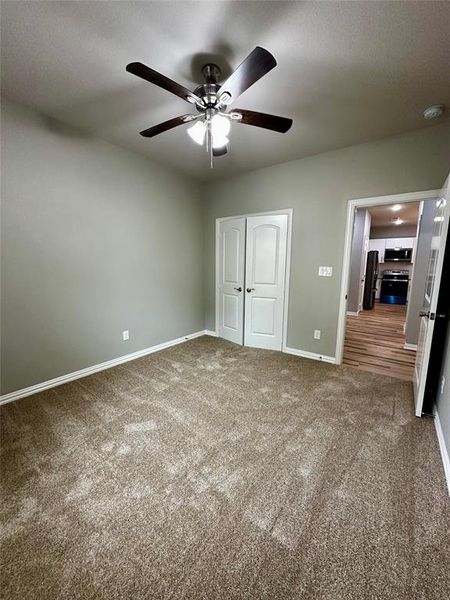 Unfurnished bedroom with carpet, ceiling fan, black fridge, and a closet