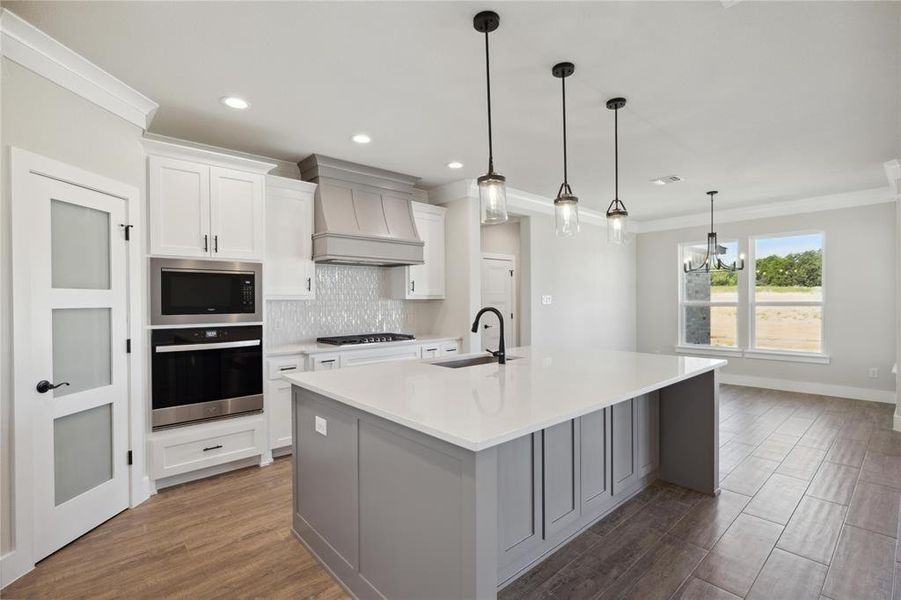 Kitchen with white cabinets, custom exhaust hood, a large island, dark wood-type flooring, and stainless steel appliances