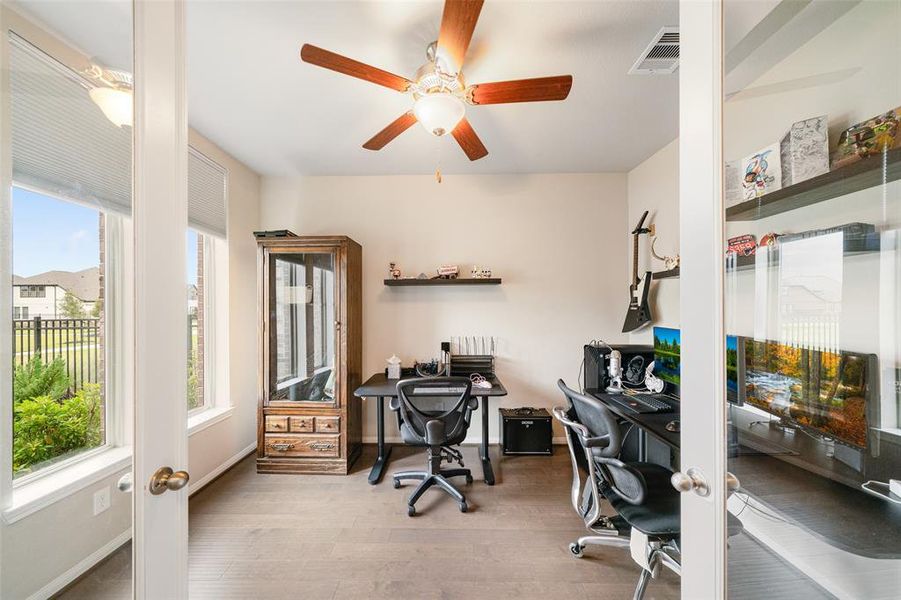 Bright, modern home office with large windows, wood flooring, and a ceiling fan.The room looks out onto a front & side yard, offering a pleasant view and natural light.