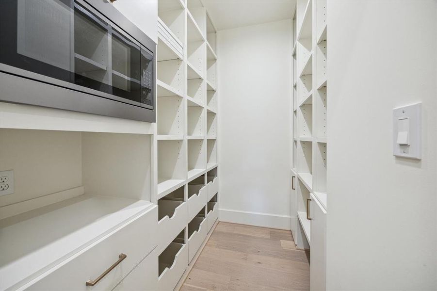 The working pantry just off the kitchen provides a beautiful place for food storage. A built-in microwave sits above a shelf that has a power outlet for small appliances which keeps kitchen counters clear and uncluttered.