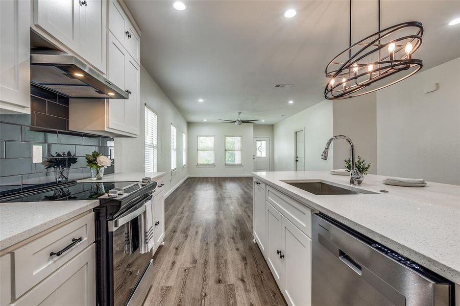 Kitchen with light hardwood / wood-style flooring, ceiling fan with notable chandelier, white cabinets, appliances with stainless steel finishes, and sink