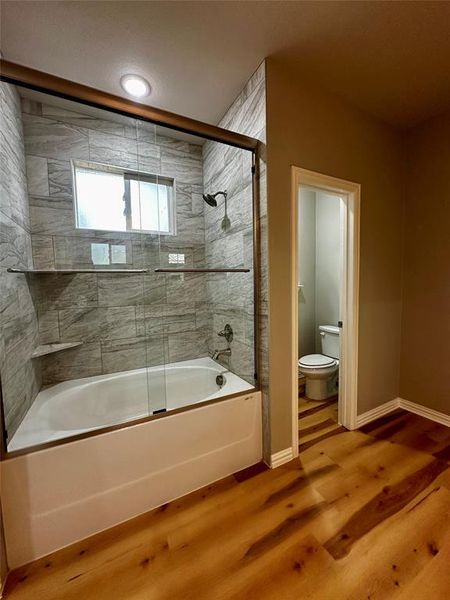 Bathroom featuring toilet, hardwood / wood-style flooring, and enclosed tub / shower combo