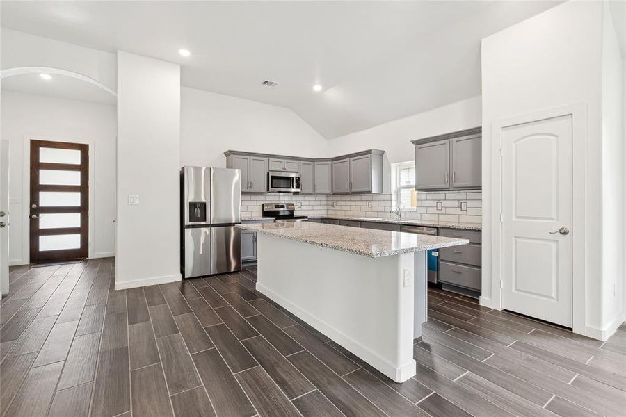 Kitchen featuring tasteful backsplash, dark hardwood / wood-style flooring, a kitchen island, appliances with stainless steel finishes, and gray cabinetry