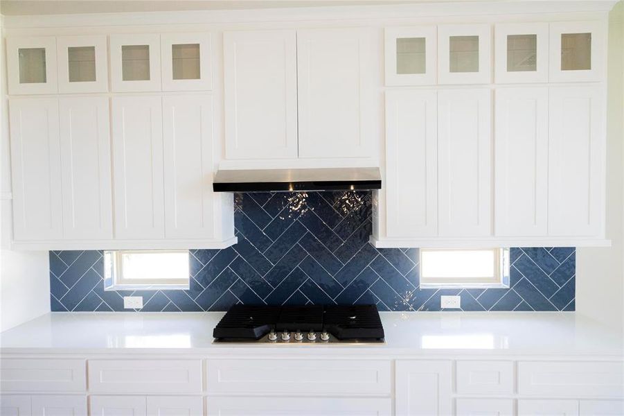 Kitchen with tasteful backsplash, white cabinets, wall chimney range hood, and gas cooktop