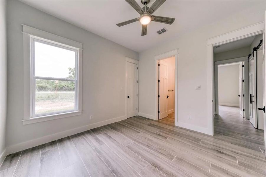 Unfurnished bedroom with ensuite bathroom, light hardwood / wood-style floors, a barn door, and ceiling fan