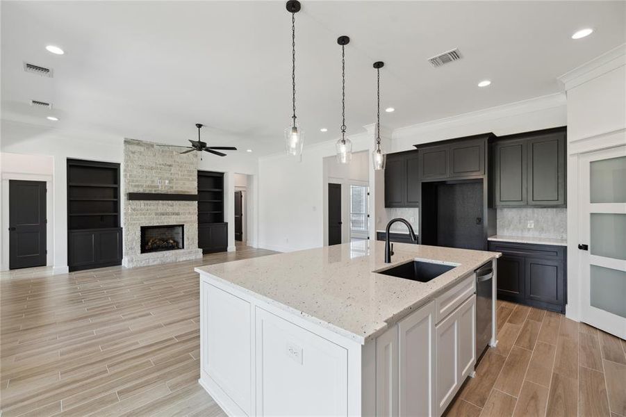 Kitchen featuring light stone countertops, sink, a stone fireplace, ceiling fan, and decorative backsplash