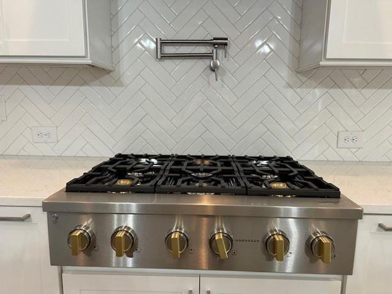 Kitchen with backsplash, light stone counters, stove, stainless steel gas cooktop, and white cabinetry