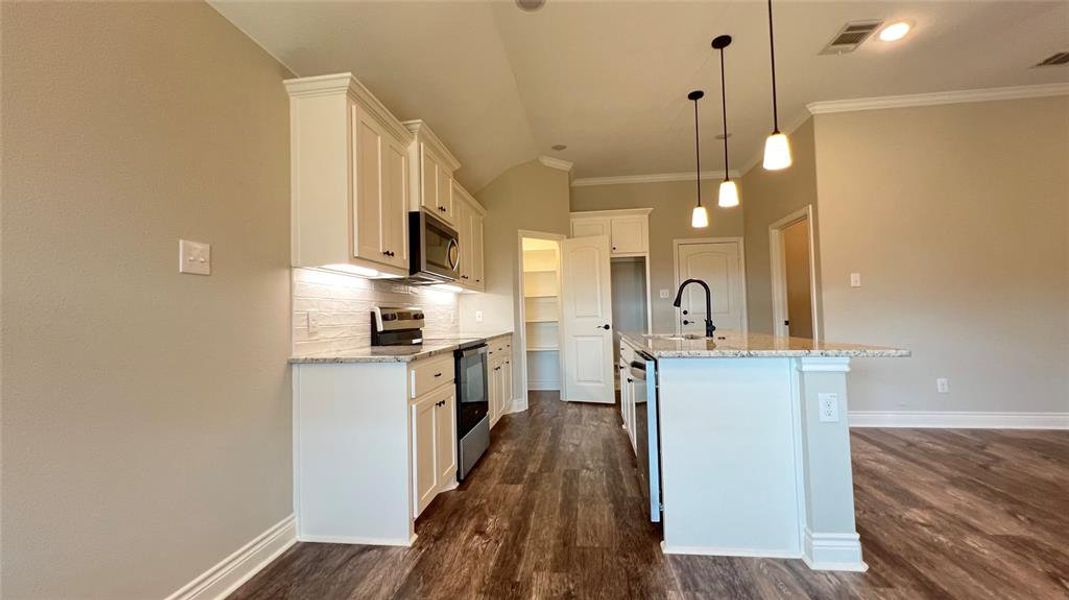 Kitchen with pendant lighting, white cabinets, sink, a center island with sink, and appliances with stainless steel finishes