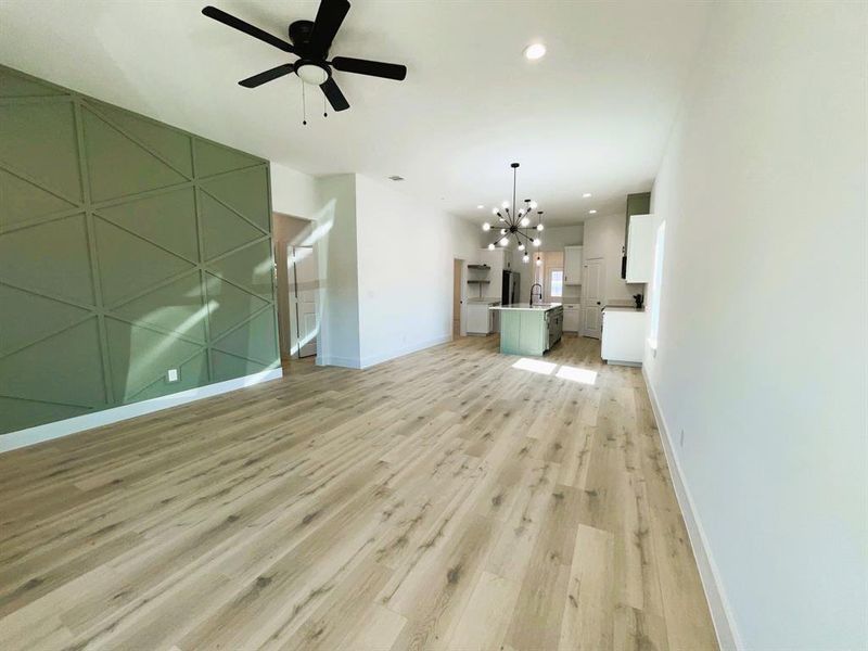 Unfurnished living room with sink, ceiling fan with notable chandelier, and light wood-type flooring