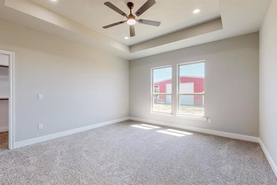 Empty room with a raised ceiling, carpet flooring, and ceiling fan