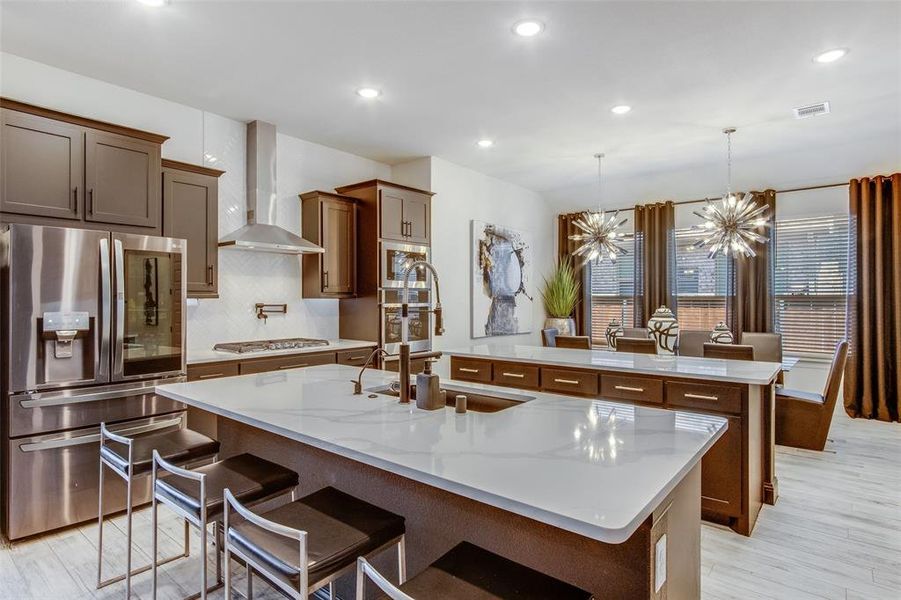 Kitchen with stainless steel appliances, a center island with sink, wall chimney exhaust hood, and a chandelier