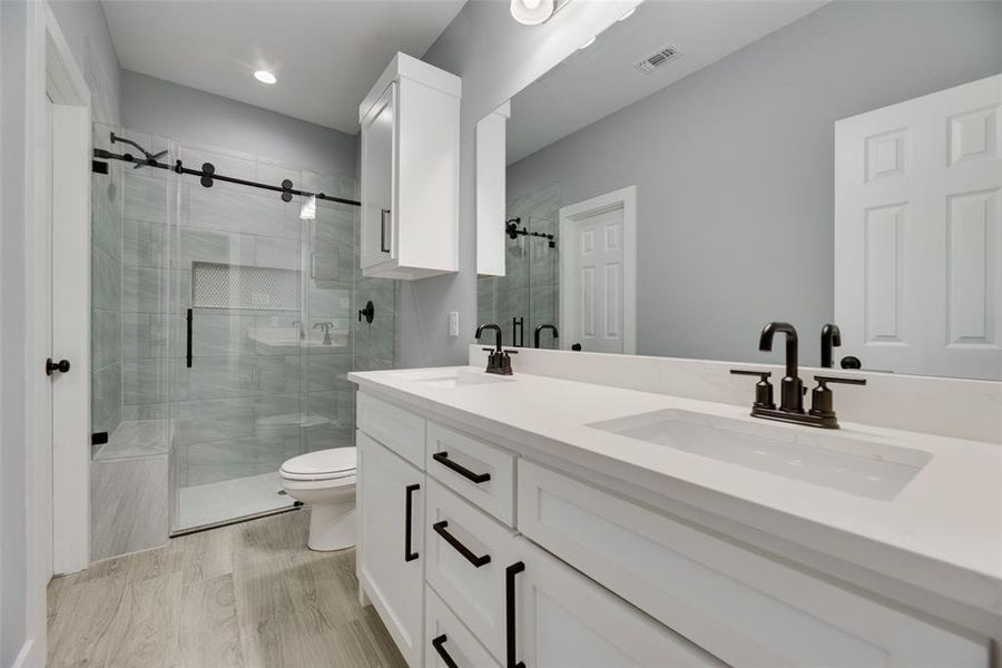 Bathroom featuring hardwood / wood-style flooring, toilet, double sink vanity, and walk in shower