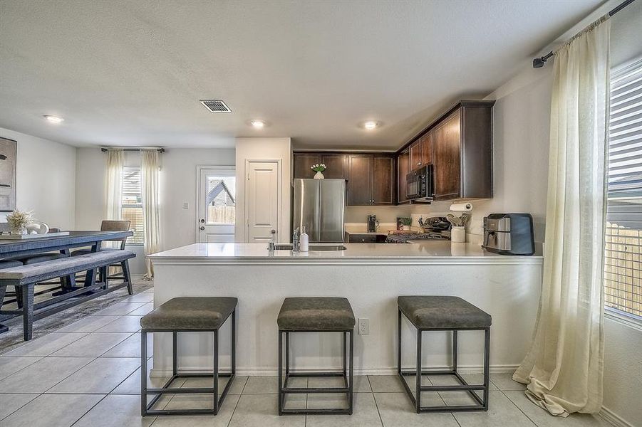 Kitchen featuring dark brown cabinets, light tile patterned flooring, a kitchen bar, and appliances with stainless steel finishes