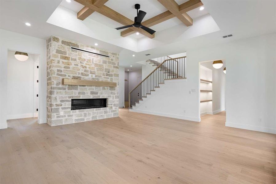 Unfurnished living room featuring light wood-type flooring, a fireplace, ceiling fan, and beamed ceiling