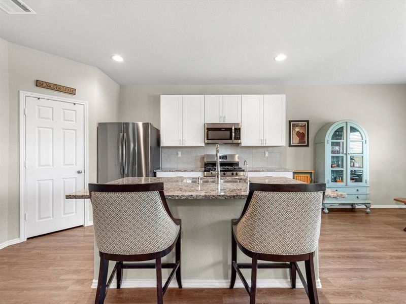 This light and bright kitchen features a large granite island, white cabinets, a large sink overlooking your family room, recessed lighting, and beautiful backsplash.