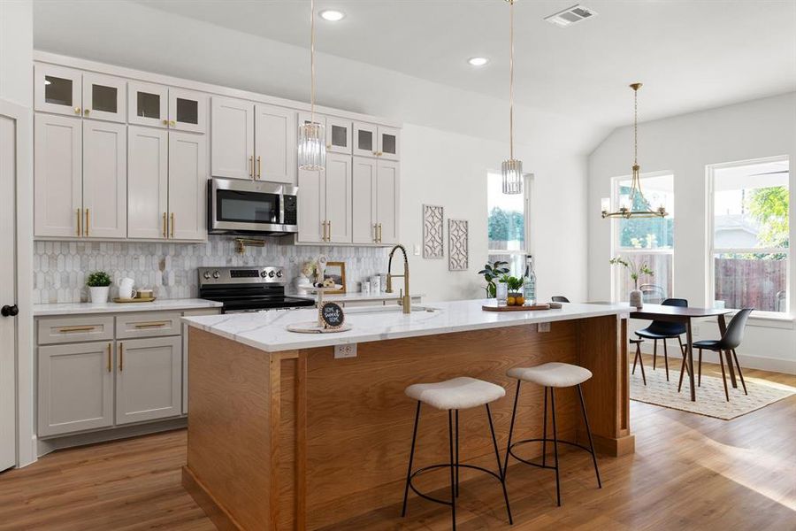 Kitchen with wood-type flooring, an island with sink, stainless steel appliances, and white cabinetry