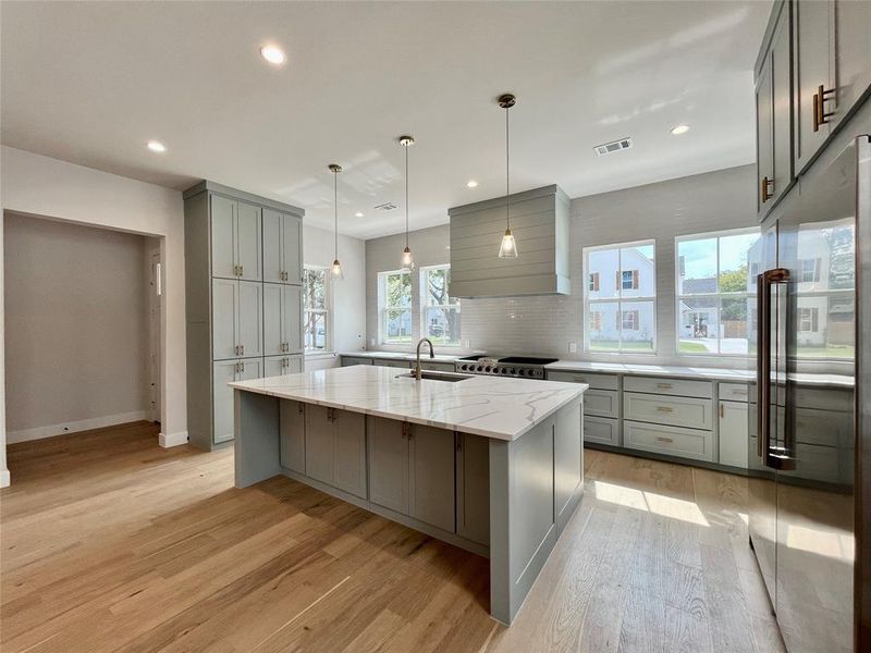 Kitchen featuring light hardwood / wood-style floors, gray cabinetry, light stone counters, appliances with stainless steel finishes, and a spacious island