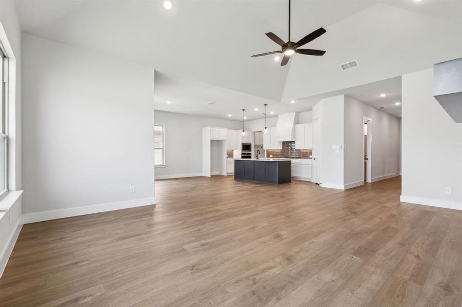 Unfurnished living room with high vaulted ceiling, ceiling fan, and light wood-type flooring