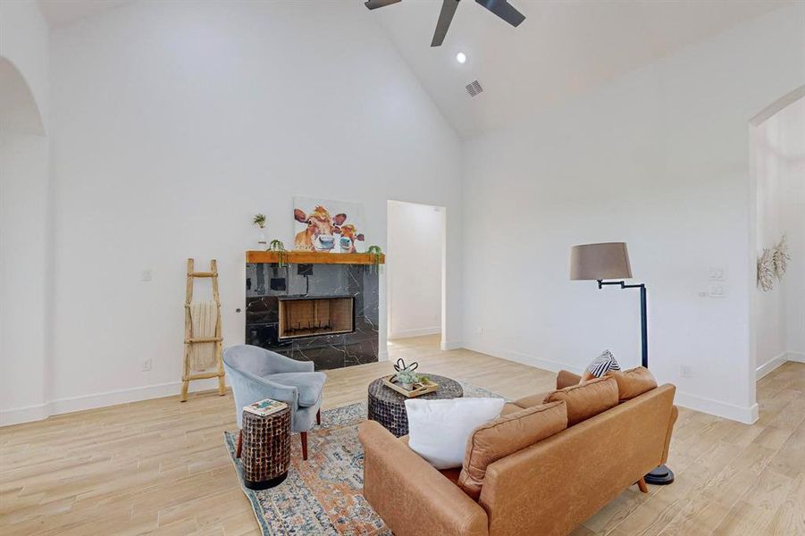 Living room with ceiling fan, a tile fireplace, light hardwood / wood-style flooring, and high vaulted ceiling