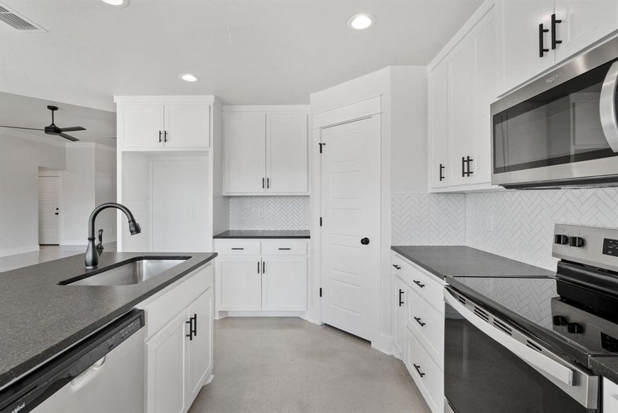 Kitchen with ceiling fan, backsplash, white cabinetry, sink, and stainless steel appliances