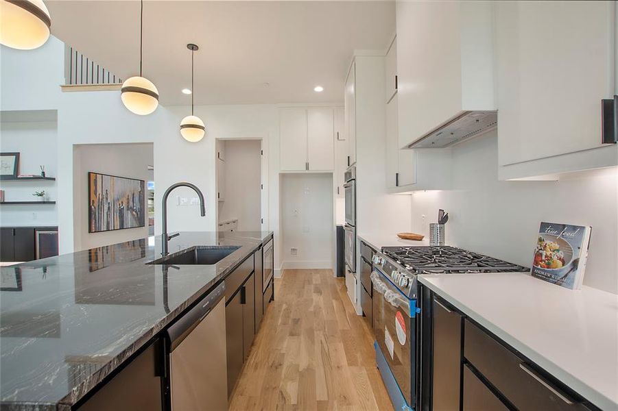 Kitchen featuring hanging light fixtures, stainless steel appliances, range hood, dark stone countertops, and white cabinets