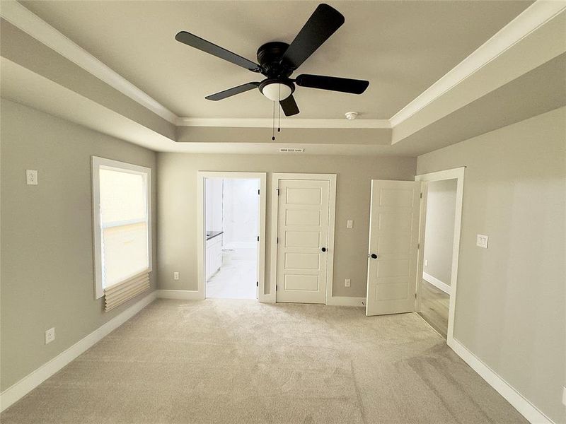 Unfurnished bedroom featuring a raised ceiling, connected bathroom, ceiling fan, and light colored carpet