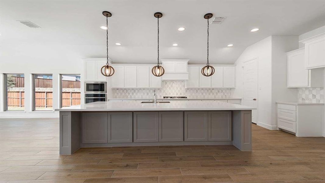 Kitchen featuring a large island with sink, white cabinets, stainless steel appliances, and wood-type flooring