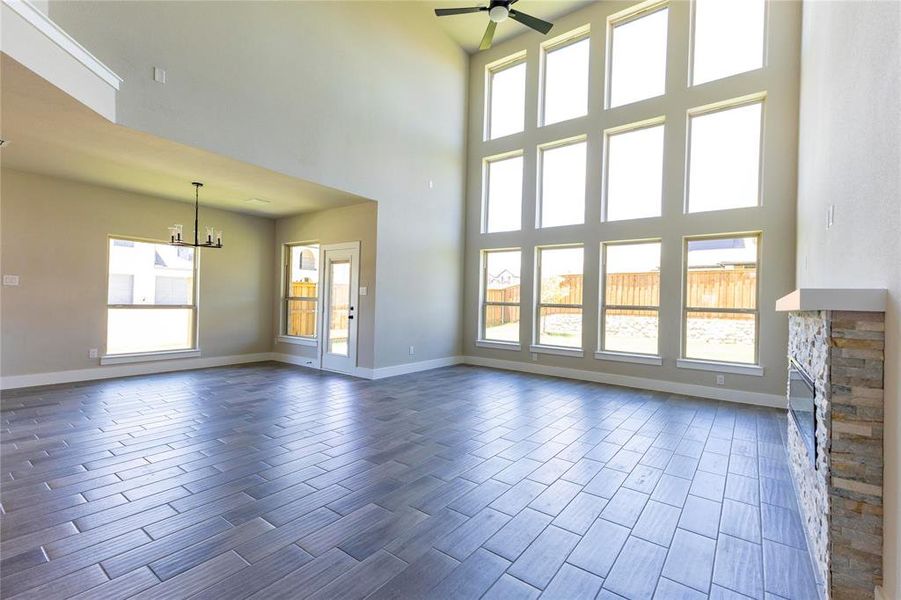 Unfurnished living room featuring a stone fireplace, ceiling fan with notable chandelier, and a towering ceiling