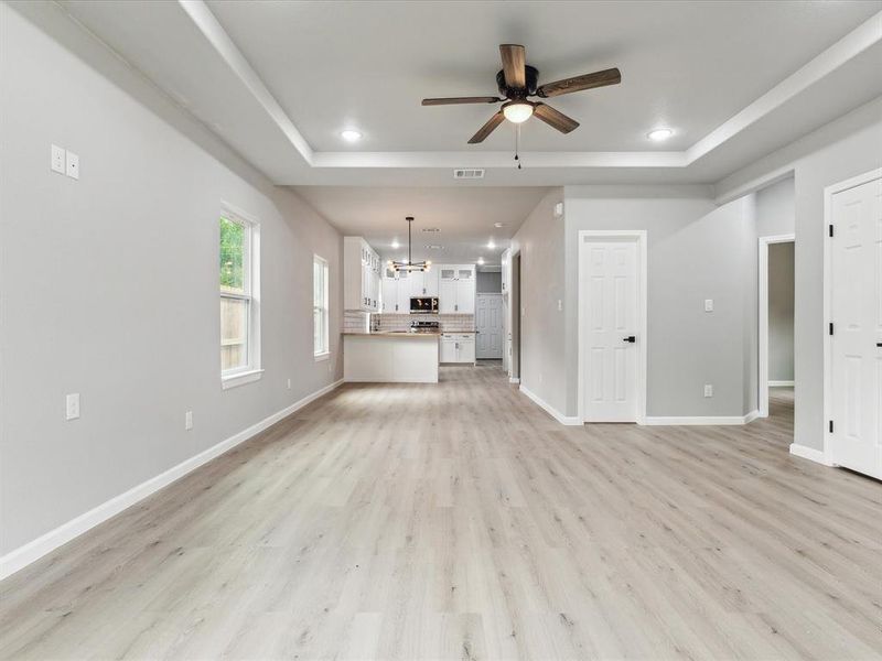 Unfurnished living room featuring ceiling fan with notable chandelier, a raised ceiling, and light hardwood / wood-style flooring