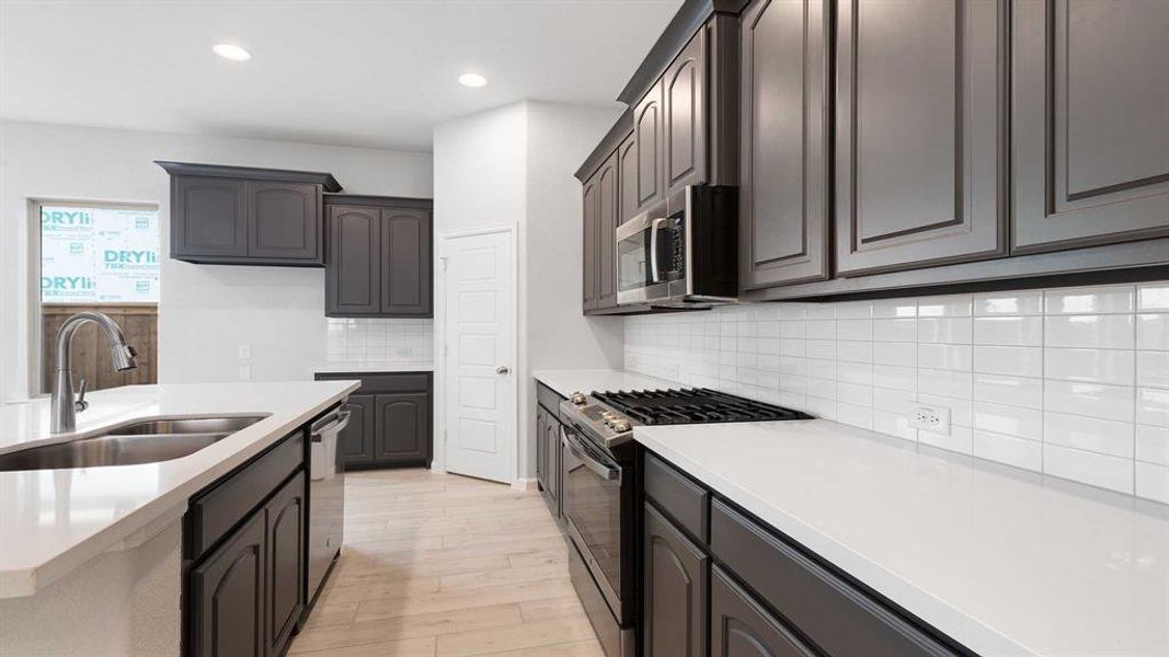 Kitchen featuring dark brown cabinets, light hardwood / wood-style floors, tasteful backsplash, sink, and stainless steel appliances