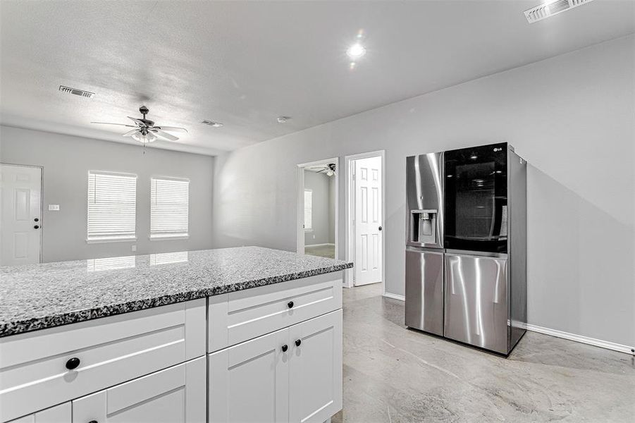 Kitchen featuring white cabinets, stainless steel fridge, light stone countertops, light tile patterned flooring, and ceiling fan