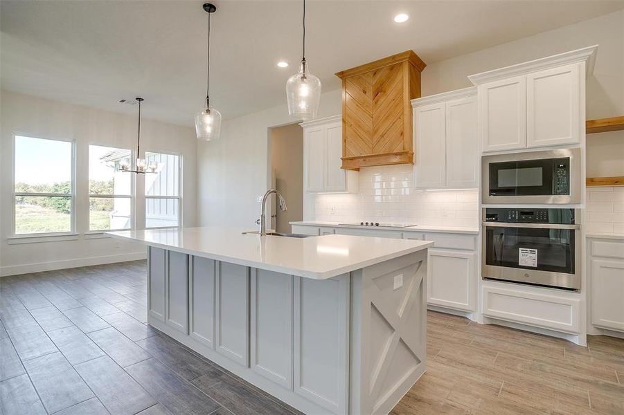 Kitchen featuring an island with sink, white cabinetry, sink, decorative light fixtures, and stainless steel appliances