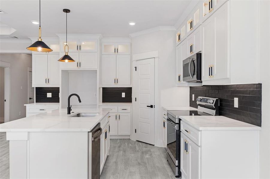 Kitchen featuring decorative light fixtures, an island with sink, stainless steel appliances, sink, and ornamental molding