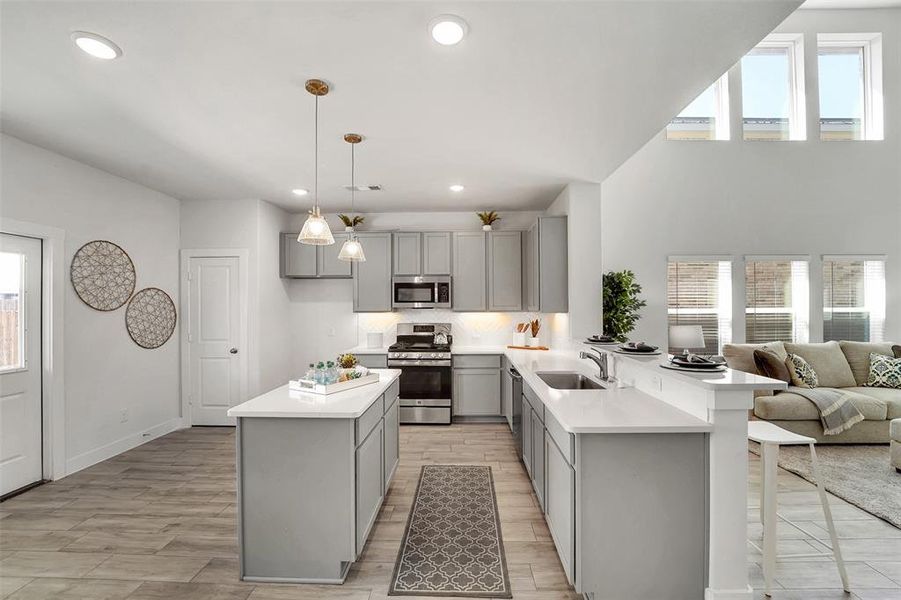 Kitchen featuring stainless steel appliances, gray cabinetry, sink, kitchen peninsula, and decorative light fixtures