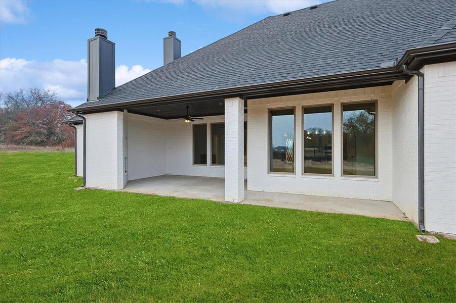 Rear view of property featuring a lawn, ceiling fan, and a patio area